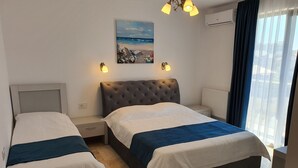 A hotel room with two beds, a painting of a beach scene, a ceiling light, and a window with curtains. - Roca del Mar (Navodari)