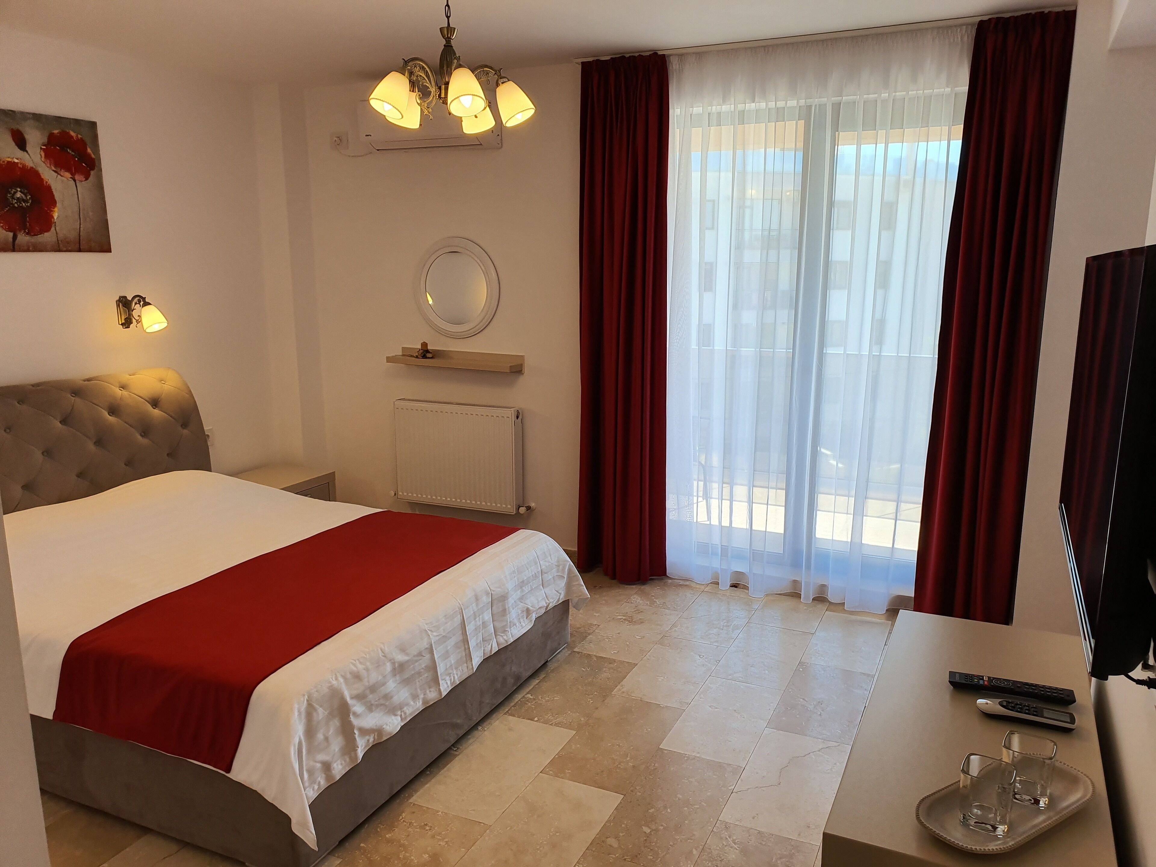 Une chambre d’hôtel avec un lit, un miroir rond, un radiateur, une télévision et une fenêtre avec des rideaux.