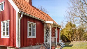 Et rødt træhus med et tag af fliser, et hvidt vindue og en lille veranda med en bænk.