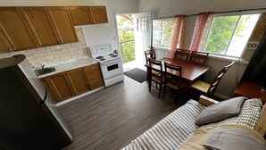 Een kleine keuken met houten kastjes, een fornuis en een eethoek met een tafel en stoelen.