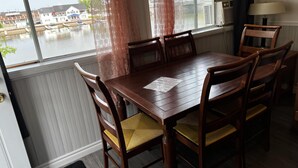 Een eetgedeelte met een tafel en stoelen, een raam met uitzicht op een gracht en gebouwen, en een airconditioner aan de muur.