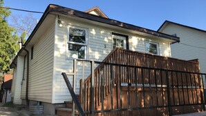 A single-story house with a wooden deck and a small front porch. - Dock Life Beach 1 - Cottage 3, Riverside 2 bedroom, 3 min walk to Beach 1 (Wasaga Beach)
