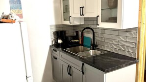 A compact kitchen with white cabinets, a black countertop, and a wooden ceiling. - Dock Life Beach 1 - Cottage 3, Riverside 2 bedroom, 3 min walk to Beach 1 (Wasaga Beach)