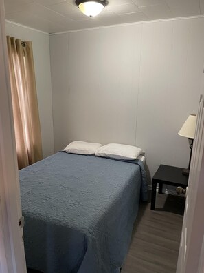 Ett sovrum med en säng, två kuddar, ett nattduksbord med en lampa och ett fönster med gardiner.