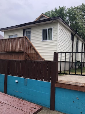 A single-story house with a wooden deck and a blue wall. - Dock Life Beach 1 - Cottage 4, Riverside 2 bedroom, 3 min walk to Beach 1 (Wasaga Beach)