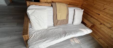 Ein rustikales Holzhaus-Interieur mit einem Bett, einer hölzernen Bank und einem gerahmten Bild an der Wand.