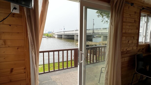 Una cabaña de madera con un toldo corredero que da a una terraza con vistas a un río.