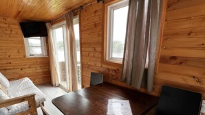 Una cabaña de madera con una mesa de comedor, dos sillas, un sofá y un ventanal con vistas a un paisaje natural.