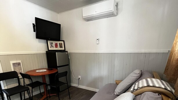 A small, neatly arranged room with a bed, a desk, a chair, and a television mounted on the wall. - Dock Life Beach 1 - Cottage 5, Riverside Property, 2 Bdrm, 3 min walk to Beach 1 (Wasaga Beach)