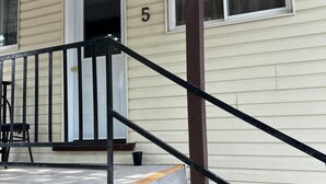 A house with a porch, a black railing, and a white door with the number 5 on it. - Dock Life Beach 1 - Cottage 5, Riverside Property, 2 Bdrm, 3 min walk to Beach 1 (Wasaga Beach)
