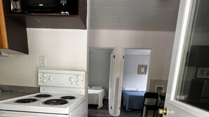 A kitchen with a white stove, a microwave, and a small dining area with a table and chairs. - Dock Life Beach 1 - Cottage 5, Riverside Property, 2 Bdrm, 3 min walk to Beach 1 (Wasaga Beach)
