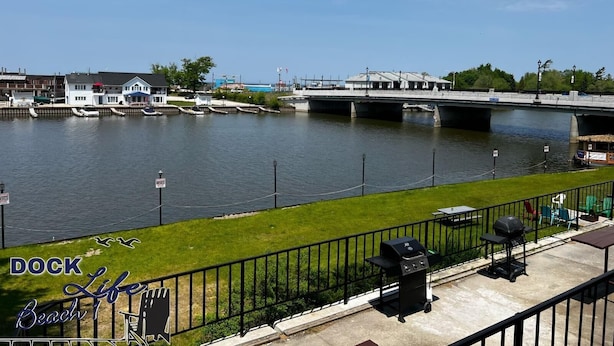 Blick auf das Wasser mit einer Anlegestelle, einer Brücke und einer Wiese mit Grillmöglichkeit.