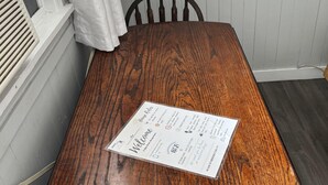 Ein Holzespeisetisch mit Platzsetzer in einem Raum mit weißen Wandverkleidungen und einem Fenster mit weißen Vorhängen.