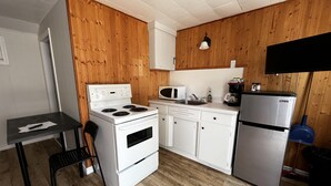 Una cucina compatta con fornelli, microonde, frigorifero e un piccolo tavolo con una sedia.