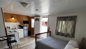 Una stanza compatta con un letto, una scrivania, una sedia, un angolo cottura e una finestra con tende.
