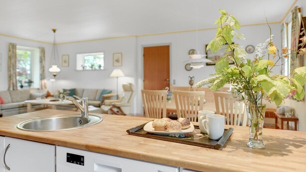 A modern kitchen with a wooden countertop, a sink, and a dining area with chairs and a table.