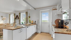 A modern kitchen with white cabinets, wooden countertops, and a large window offering a view of the outdoors.