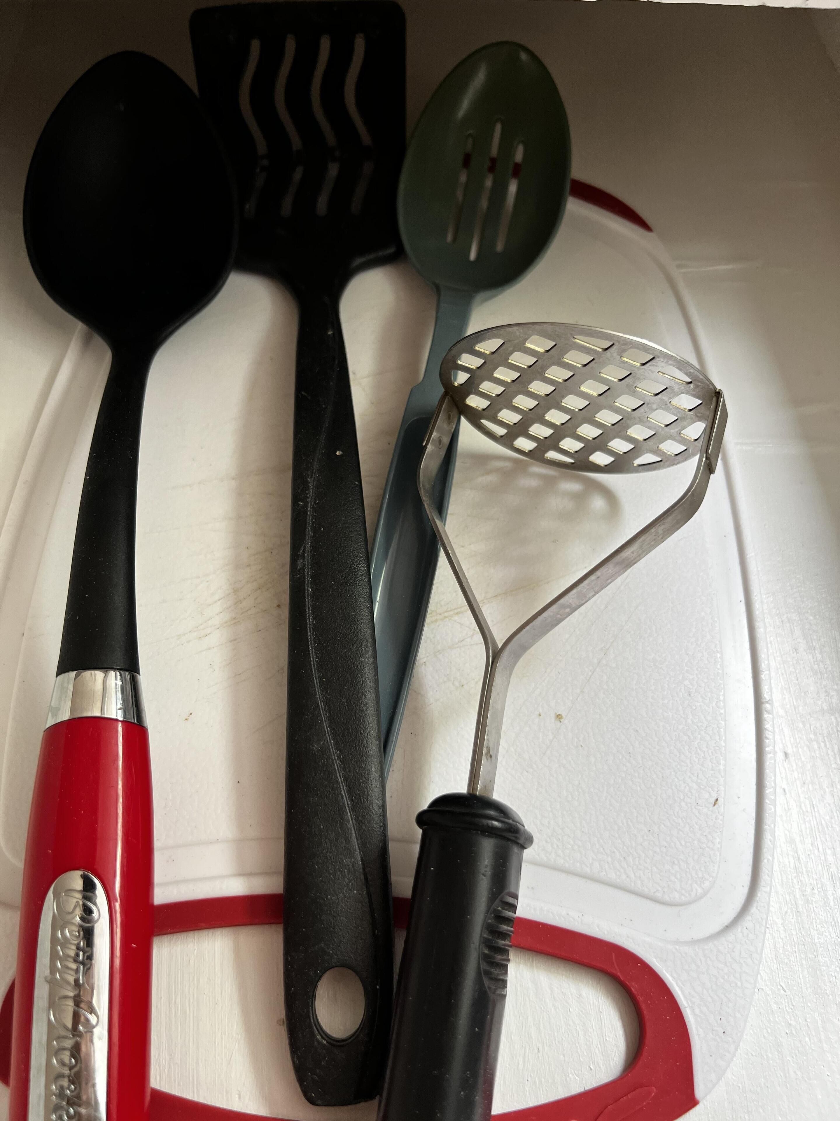 Un plan de travail de cuisine avec divers ustensiles, notamment une louche rouge, une spatule noire, une autre spatule verte et une passoire en métal.