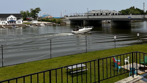A river with a boat, a bridge, and a grassy area with a fence and chairs. - Dock Life Beach 1 - Cottage 9, Riverside Property, Studio, 3 min walk to Beach 1 (Wasaga Beach)
