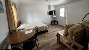 A compact room with a bed, a small table, and a chair. There's a television mounted on the wall and a door with a window. - Dock Life Beach 1 - Cottage 9, Riverside Property, Studio, 3 min walk to Beach 1 (Wasaga Beach)