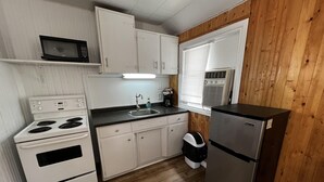 A compact kitchen with white cabinets, a microwave, a stove, a sink, and a refrigerator. - Dock Life Beach 1 - Cottage 9, Riverside Property, Studio, 3 min walk to Beach 1 (Wasaga Beach)