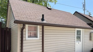 A small, single-story house with a brown roof, a white door, and a window with a curtain. - Dock Life Beach 1 - Cottage 9, Riverside Property, Studio, 3 min walk to Beach 1 (Wasaga Beach)