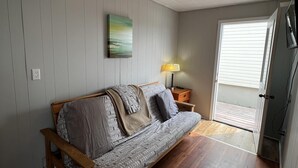 Una habitación con sofá de madera, lámpara, un cuadro y una puerta que da al exterior.