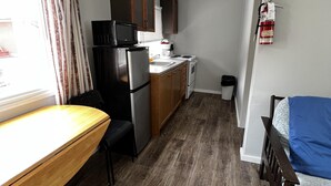 Una cocina compacta con refrigerador, microondas y estufa. Hay una mesa de madera y un banco. Un extintor está montado en la pared.