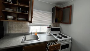 Cocina compacta con lavamanos, estufa y armarios abiertos.