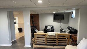 Un salon doté d’une cheminée, de deux canapés en cuir noir, d’un banc en bois et d’un téléviseur fixé au mur.