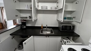 A compact kitchen with white cabinets, a black countertop, a stainless steel sink, a microwave, and a stove. - Dock Life Beach 1 - Unit 16, Riverside Property, 2 Bdrm, 3 min walk to Beach 1 (Wasaga Beach)