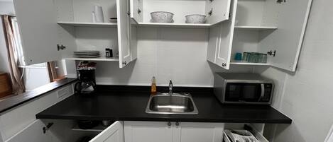 A compact kitchen with white cabinets, a black countertop, a stainless steel sink, a microwave, and a stove.