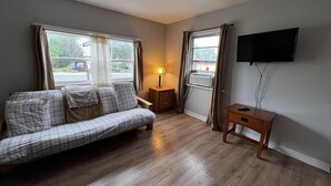 A room with a sofa, a small table, a lamp, and a TV mounted on the wall. - Dock Life Beach 1 - Unit 16, Riverside Property, 2 Bdrm, 3 min walk to Beach 1 (Wasaga Beach)