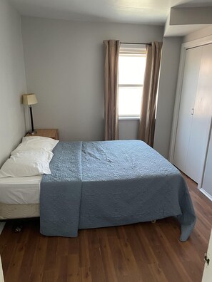 A bedroom with a bed, a nightstand, a lamp, a window with curtains, and a door. - Dock Life Beach 1 - Unit 16, Riverside Property, 2 Bdrm, 3 min walk to Beach 1 (Wasaga Beach)