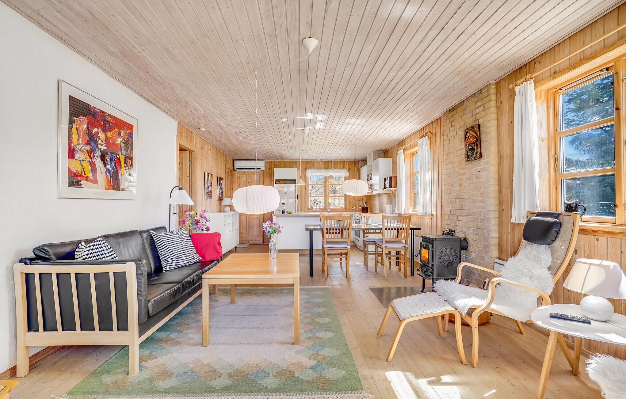 Un salon moderne avec un plafond en bois, un canapé en cuir noir, une table à manger et une cheminée.