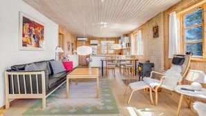 Ein modernes Wohnzimmer mit Holzbalkendecke, einem schwarzen Ledersofa, einem Esstisch und einem Kamin.