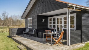 Eine Holzhütte mit einer Holzterrasse, einem Essbereich mit Stühlen und Tisch sowie einem großen Fenster mit einer Flagge.