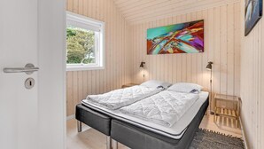 Un dormitorio con una cama, una ventana, un cuadro y una mesita de noche.