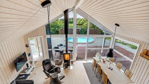 Amplia sala de estar con un gran ventanal, chimenea, piscina y comedor.