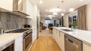 A modern kitchen with a central island, stainless steel appliances, and a wooden floor. - Duff's Cottage-fabulous location-comfort +style (Arrowtown)