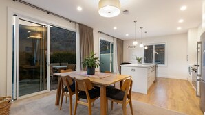 A modern kitchen with a dining area, large windows, and a view of the outdoors. - Duff's Cottage-fabulous location-comfort +style (Arrowtown)
