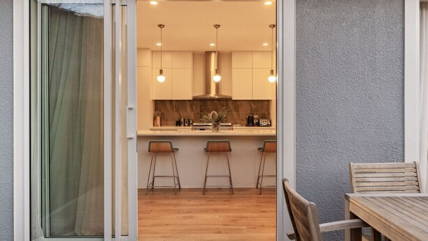 A modern kitchen with a sliding glass door leading to a dining area with wooden furniture. - Duff's Cottage-fabulous location-comfort +style (Arrowtown)