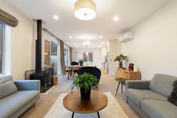 A modern living room with a sofa, a coffee table, and a dining area with a table and chairs. - Duff's Cottage-fabulous location-comfort +style (Arrowtown)