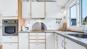 Una cocina moderna con armarios blancos, horno empotrado, cafetera y un amplio ventanal.