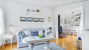 Una habitación de paredes blancas con un sofá azul, una mesita con un frutero y una lámpara blanca.