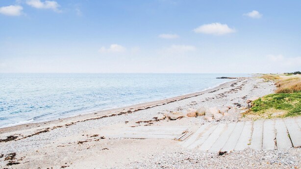 Una playa con cielo despejado, orilla de arena y un paseo marítimo de madera que lleva al agua.