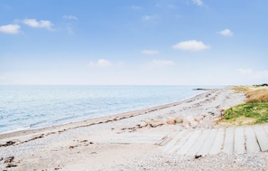 Una playa con cielo despejado, orilla de arena y un paseo marítimo de madera que lleva al agua.