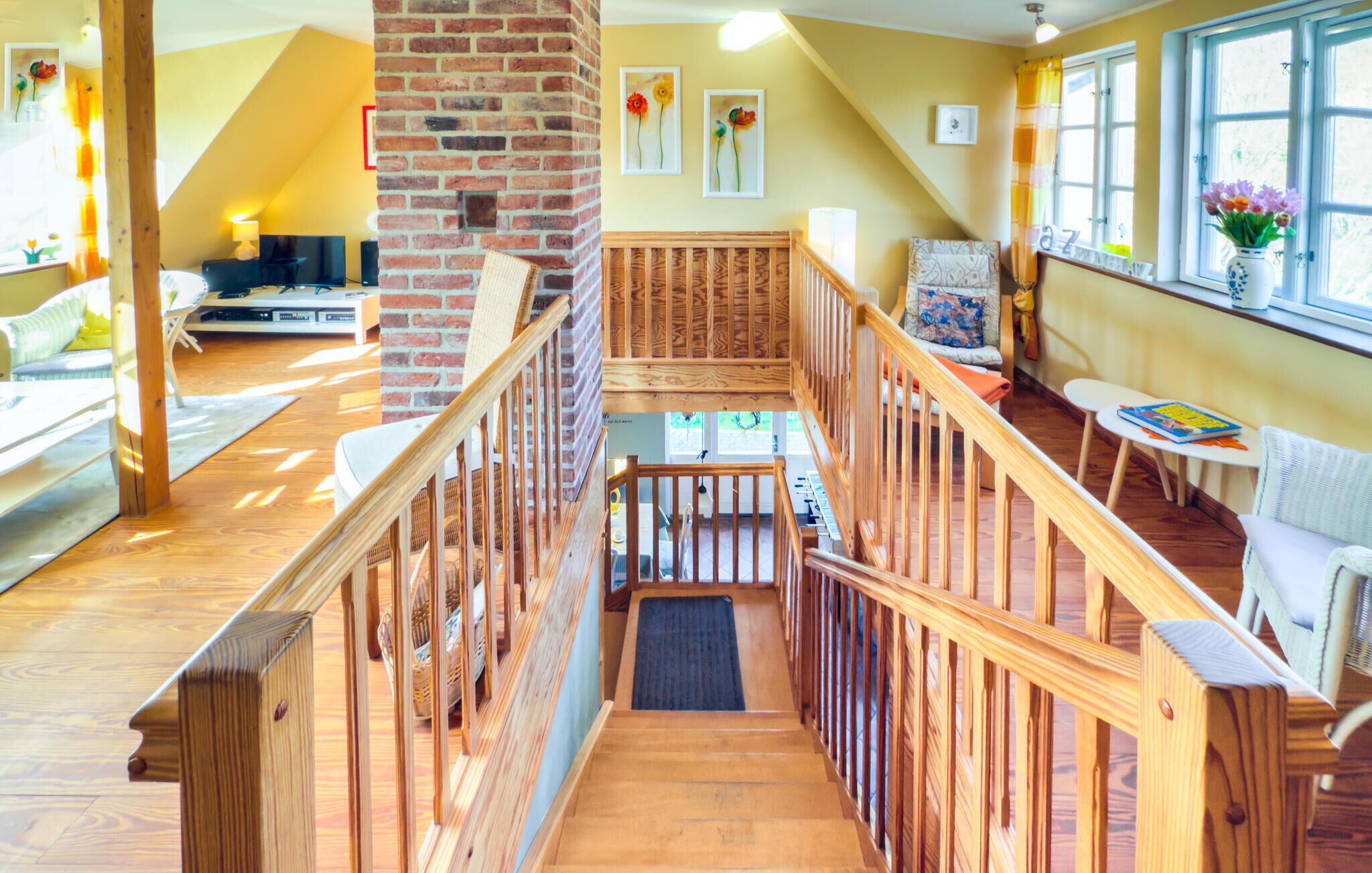 Een ruime loft-achtige kamer met een houten trap, een bakstenen open haard en een gezellige zithoek met een tafel en stoelen.