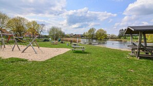 A park with playground equipment, picnic tables, a wooden shelter, and a lake. - 3 bedroom beautiful home in Thandorf (Thandorf)