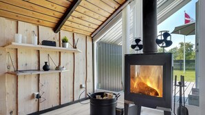 Un interior moderno con una estufa de leña, estantes de madera con objetos decorativos y vistas al exterior.